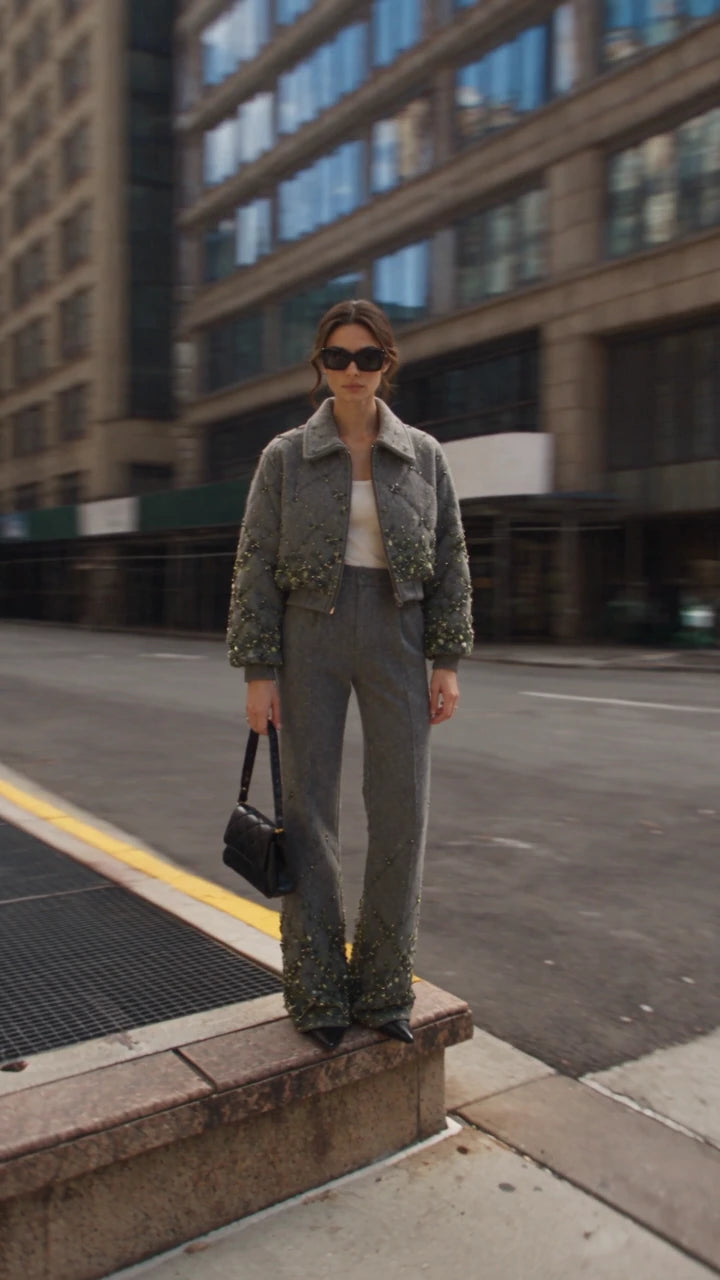 A woman wearing a grey jacket and trousers on a city street.